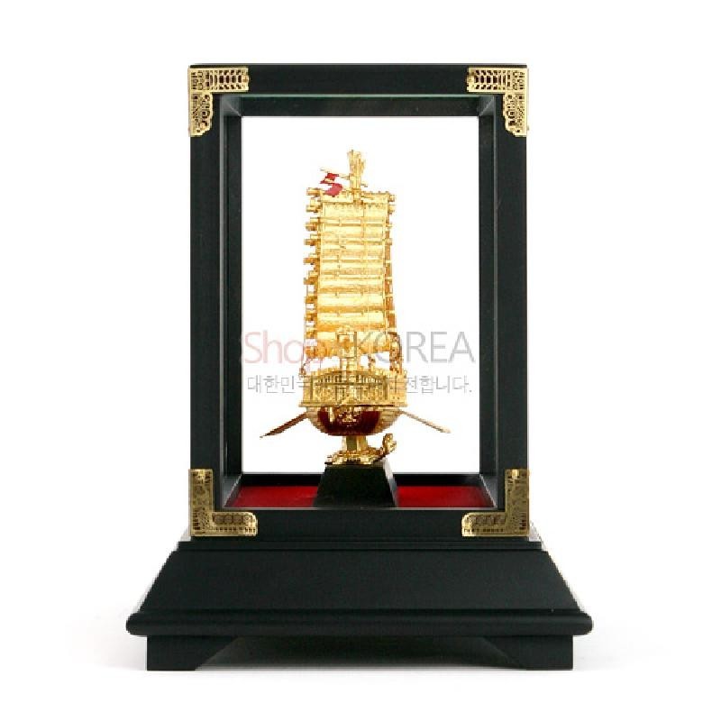 금속 재질 금도금 거북선 조형물과 흑색 목재 액자형 받침, 모서리 금속 장식이 어우러진 장식품.