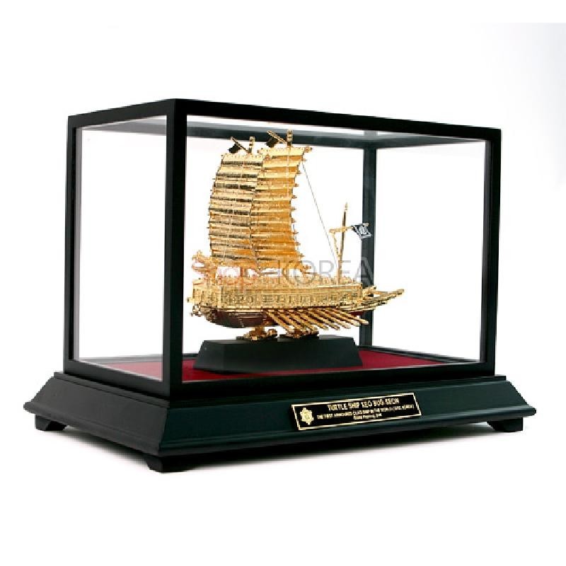 금도금 금속으로 정교하게 제작된 거북선 모형과 투명 유리 케이스, 검정 받침대 구조의 장식품. 금도금 금속으로 정교하게 제작된 거북선 모형과 투명 유리 케이스, 검정 받침대 구조의 장식품.