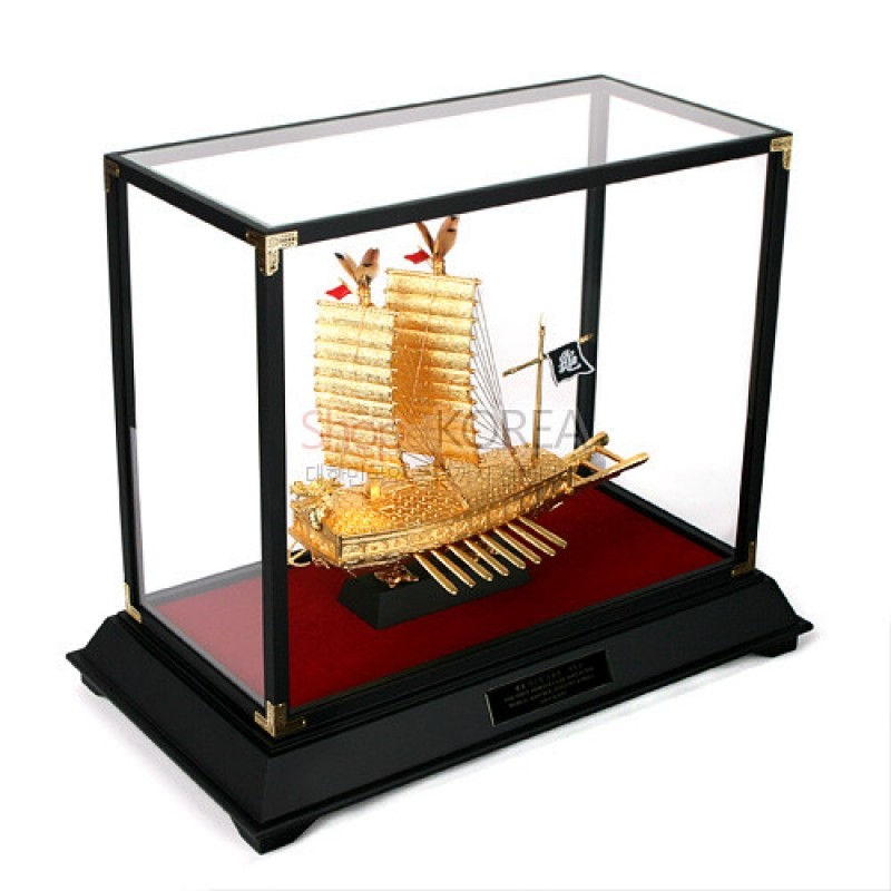 금도금 금속으로 제작된 거북선 모형과 흑색 목재 받침, 투명 유리 케이스가 조합된 장식품.
