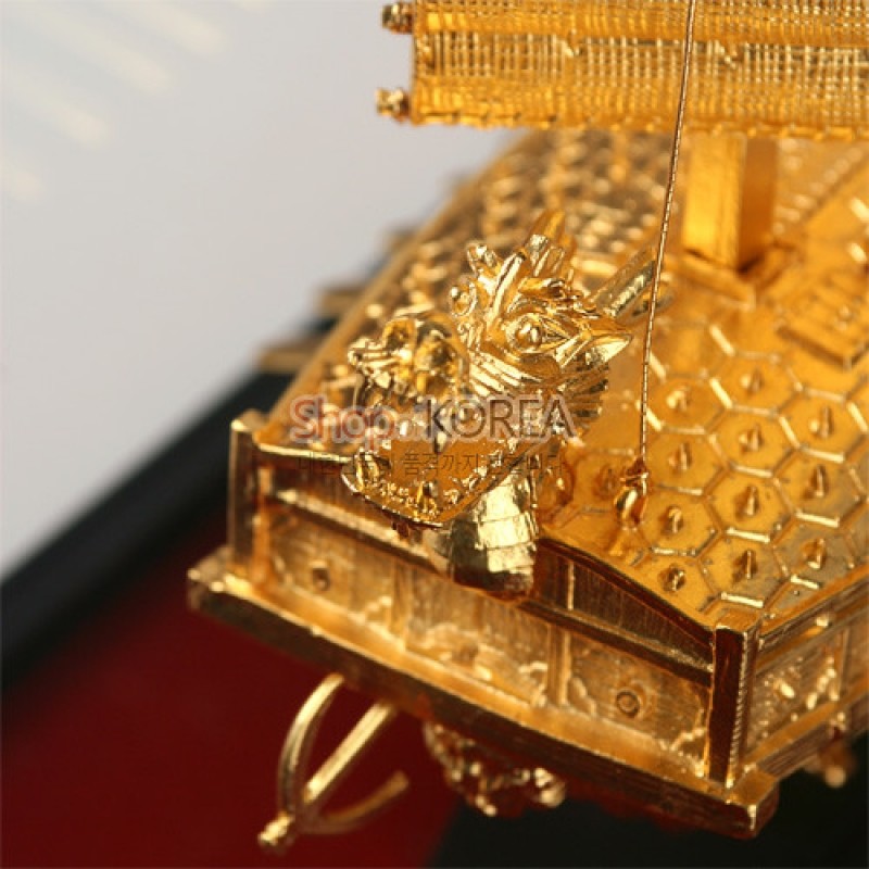 황금색 금속 재질로 제작된 거북선 모형, 육각 무늬 갑판과 정교한 용두 조각 장식이 돋보이는 공예품.