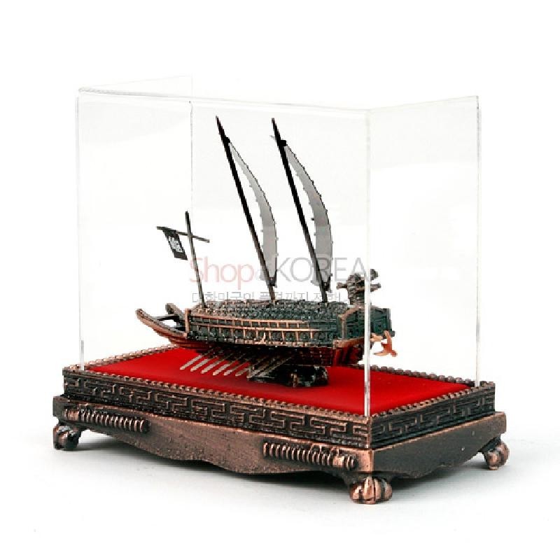 금속 재질의 동거북선 모형과 붉은 천 바닥, 투명 아크릴 케이스, 전통 문양 장식 받침대가 어우러진 장식품.