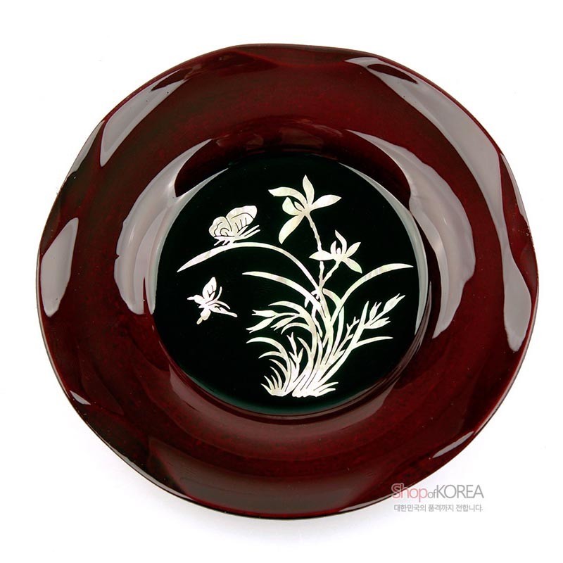 진한 와인빛 옻칠 바탕에 자개 상감 기법으로 표현한 난초와 나비 문양이 돋보이는 원형 컵받침.
