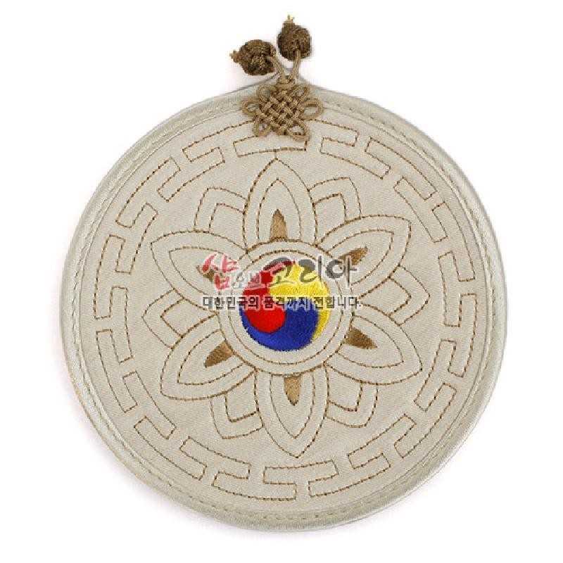 연한 베이지 천에 누비 기법으로 연꽃과 기하학 문양을 수놓고 중앙에 삼색 태극 문양을 넣은 원형 컵받침.