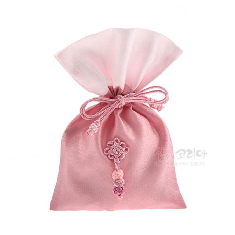 연분홍 색상의 천으로 만든 복주머니로, 입구를 끈으로 묶고 앞면에 전통 매듭 장식과 작은 매듭 문양을 더한 디자인이다.
