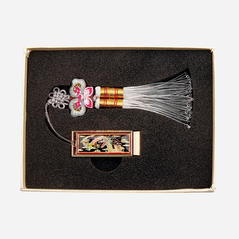 자개 상감으로 용 문양을 넣은 금속 USB 본체와 분홍·회색 비단 나비매듭, 흰 술 장식이 조화된 전통 매듭 USB.