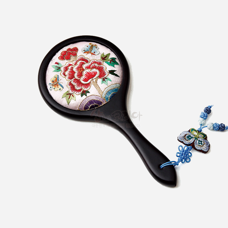 연분홍 비단 바탕 위에 붉은 꽃과 나비 자수 문양이 수놓인 원형 손거울, 청색 나비 매듭 장식이 달린 디자인.