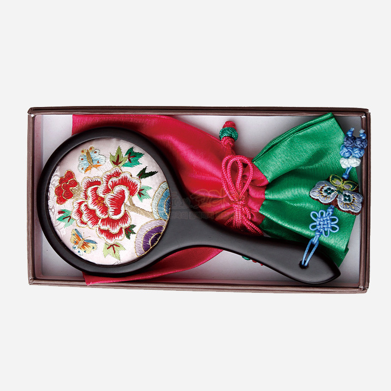 연분홍 비단 바탕에 모란과 나비 자수 문양이 놓인 손거울과, 녹색·분홍 비단 주머니에 나비 매듭 장식이 더해진 구성.