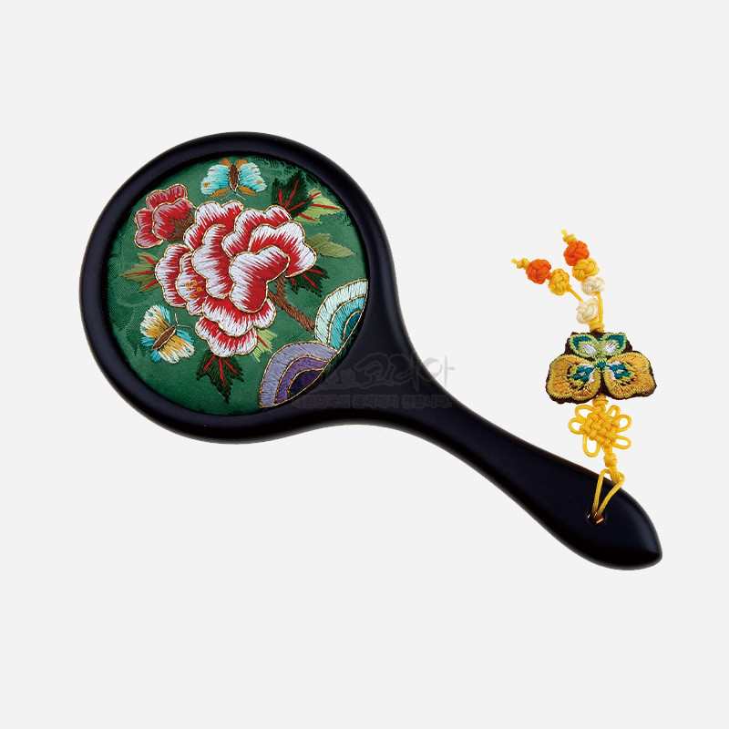 연두색 비단 바탕에 붉은 채색의 모란 자수 문양이 놓인 손거울, 노란색 전통 매듭과 복주머니 자수 장식 특징.