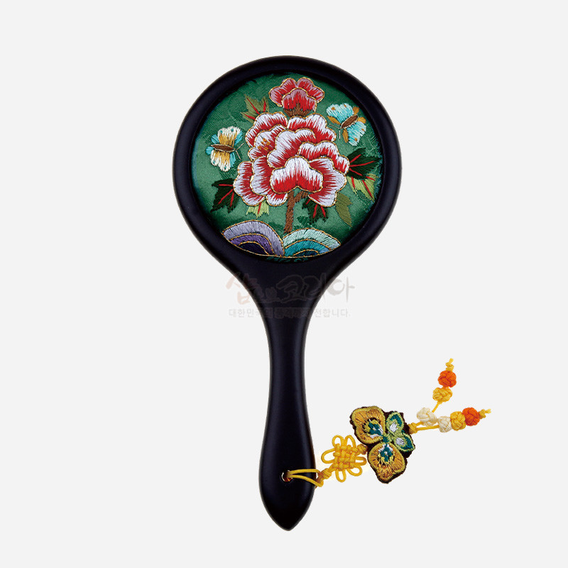 연두색 비단 바탕에 붉은 모란과 나비 자수 문양이 놓인 원형 손거울, 매끄러운 흑색 손잡이와 노랑 매듭술 장식 특징.