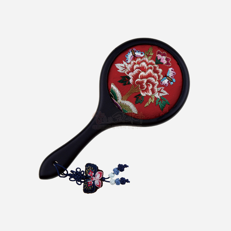 붉은 비단 바탕에 수놓은 모란과 나비 문양이 돋보이는 원형 손거울, 매듭 장식이 달린 디자인.