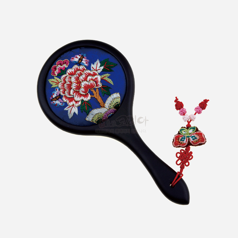 청색 바탕에 화려한 자수로 수놓은 모란과 나비 문양이 특징인 손잡이 거울과 나비 매듭 장식.