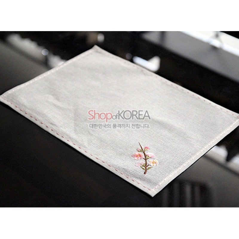 옅은 회색 모시 원단에 가장자리 색실 스티치와 한쪽 모서리 사군자 자수 꽃무늬가 더해진 식탁보.