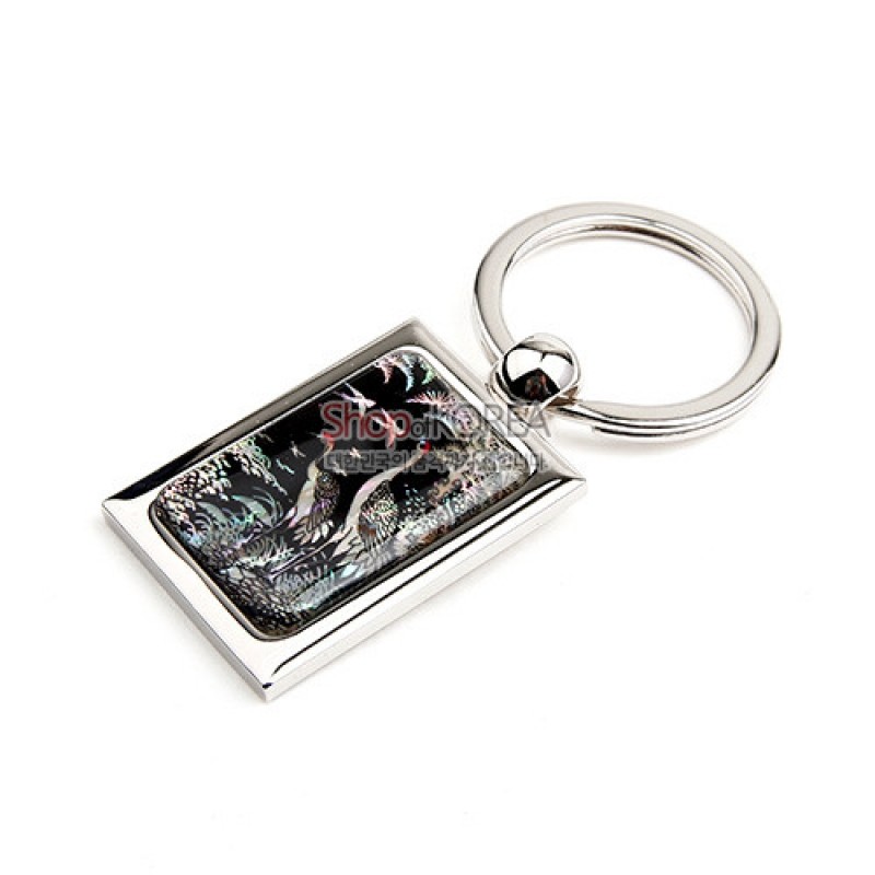 은색 금속 테두리에 흑색 바탕 자개 상감 송학 문양이 들어간 직사각형 키링 형태의 장식.