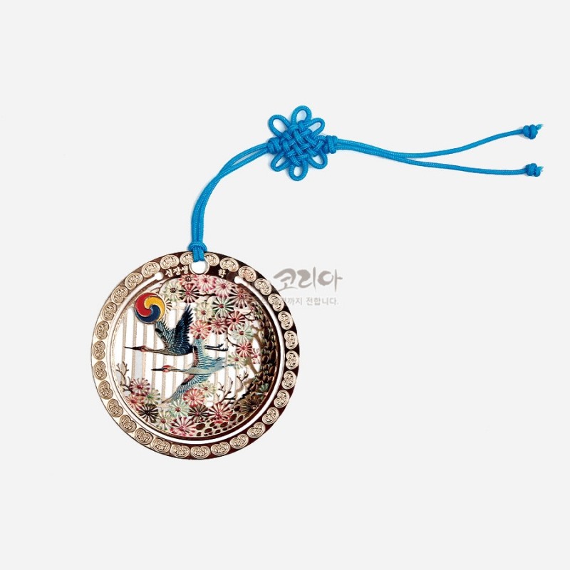 금속 바탕에 자개 상감 기법으로 십장생 학과 해, 송죽문을 표현한 둥근 책갈피와 청색 전통 매듭 끈 장식.