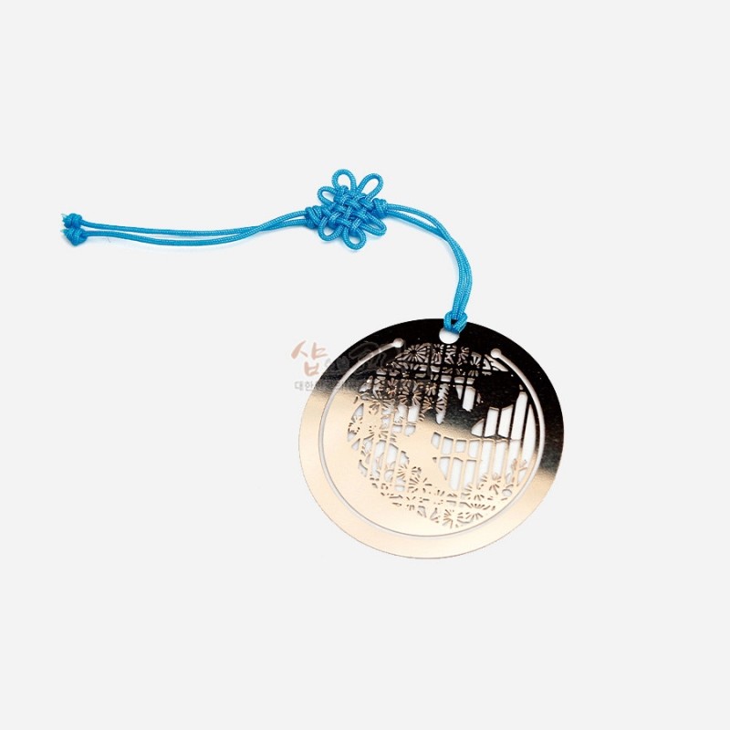 금색 금속 재질의 원형 책갈피와 청색 끈 매듭 장식, 십장생 투각 문양이 돋보이는 디자인. 금색 금속 재질의 원형 책갈피와 청색 끈 매듭 장식, 십장생 투각 문양이 돋보이는 디자인.