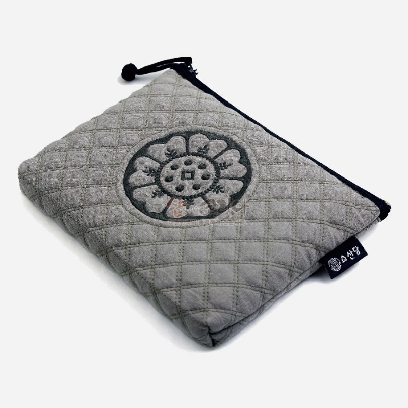 회색 누빔 원단 위에 흑색 백제 수막새 문양 자수와 검정 테두리, 스트랩 장식 파우치. 회색 누빔 원단 위에 흑색 백제 수막새 문양 자수와 검정 테두리, 스트랩 장식 파우치.