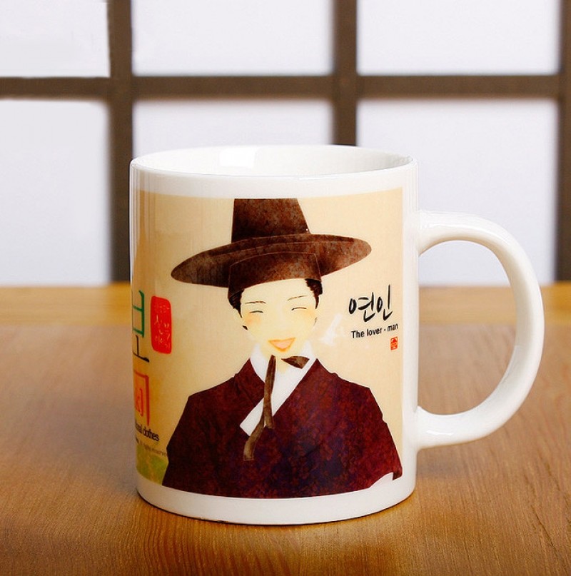 전통 한복과 갓을 쓴 남성 일러스트가 인쇄된 도자기 머그컵, 베이지 바탕에 붉은 갈색과 흰색 대비가 돋보이는 디자인.