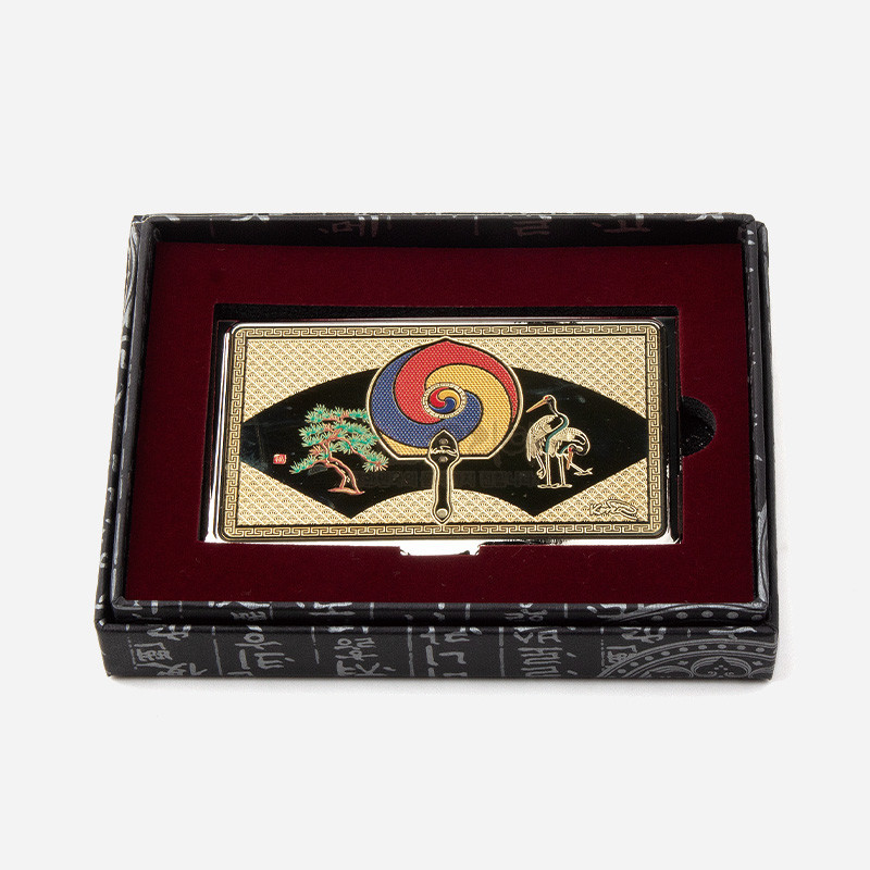 금속 재질에 금장 처리된 바탕에 태극부채와 송학문, 기하학 무늬가 채색된 명함케이스.