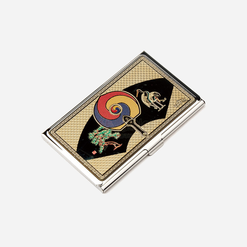 금속 재질 위에 금장 배경을 두고 태극부채, 학과 소나무 문양을 칠보 기법으로 장식한 명함케이스.