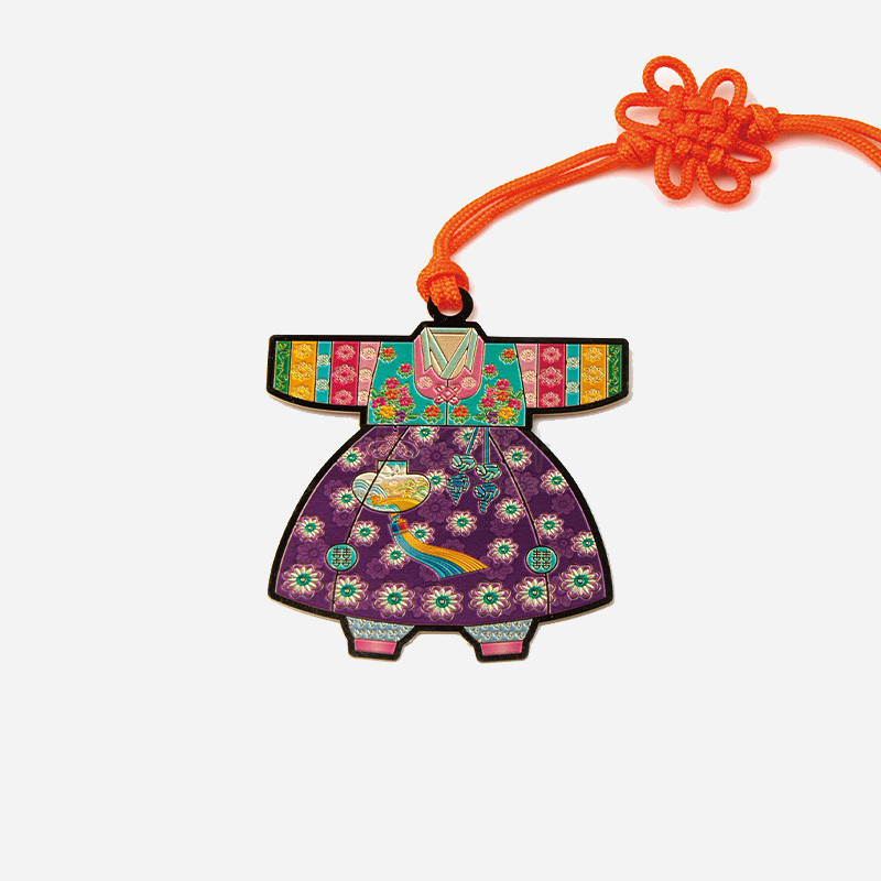 금속 재질에 아동 색동한복 형태를 담고, 자개 느낌의 화려한 꽃문양과 태슬 장식, 주황색 전통 매듭끈이 더해진 책갈피.