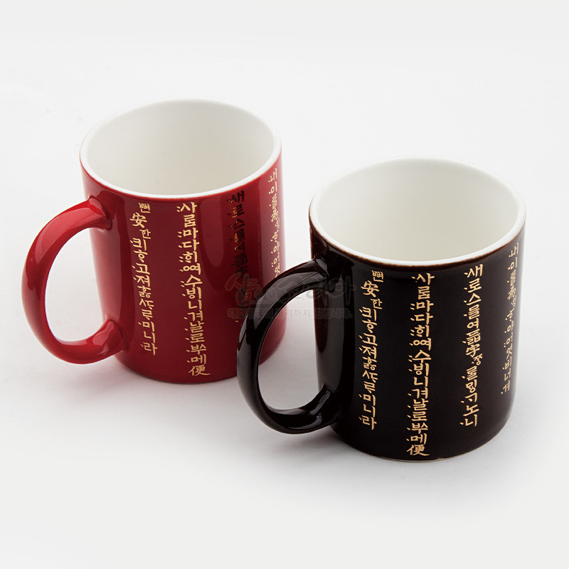붉은색과 검은색 도자기 머그컵에 황금색 훈민정음 서체가 세로로 인쇄된 디자인의 머그컵 세트.