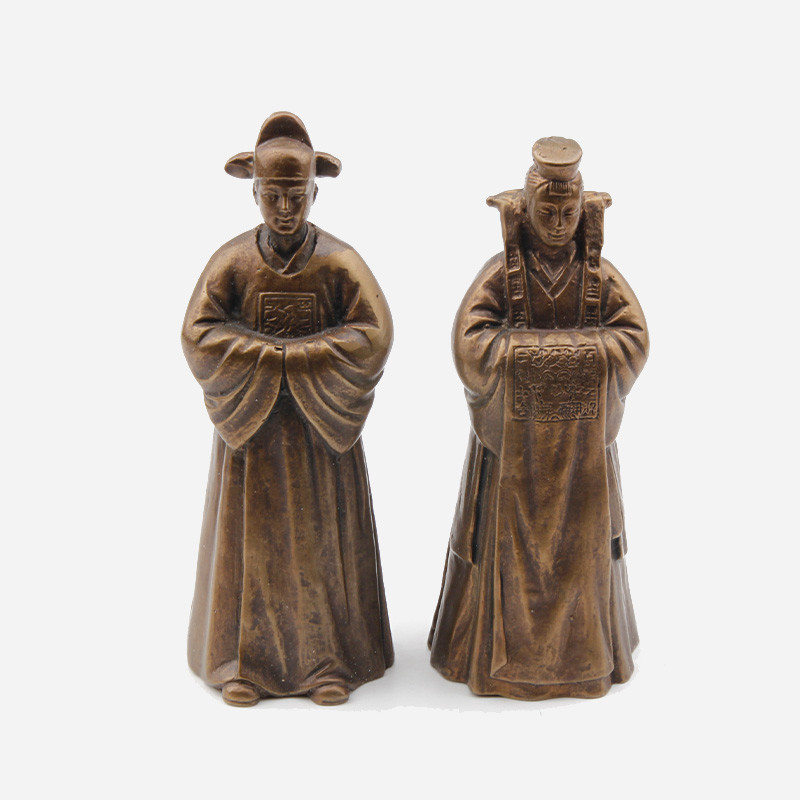 청동 재질로 제작된 전통 혼례 복식의 신랑신부 조각 종, 가슴 부분 세밀한 문양 장식이 특징인 장식품.