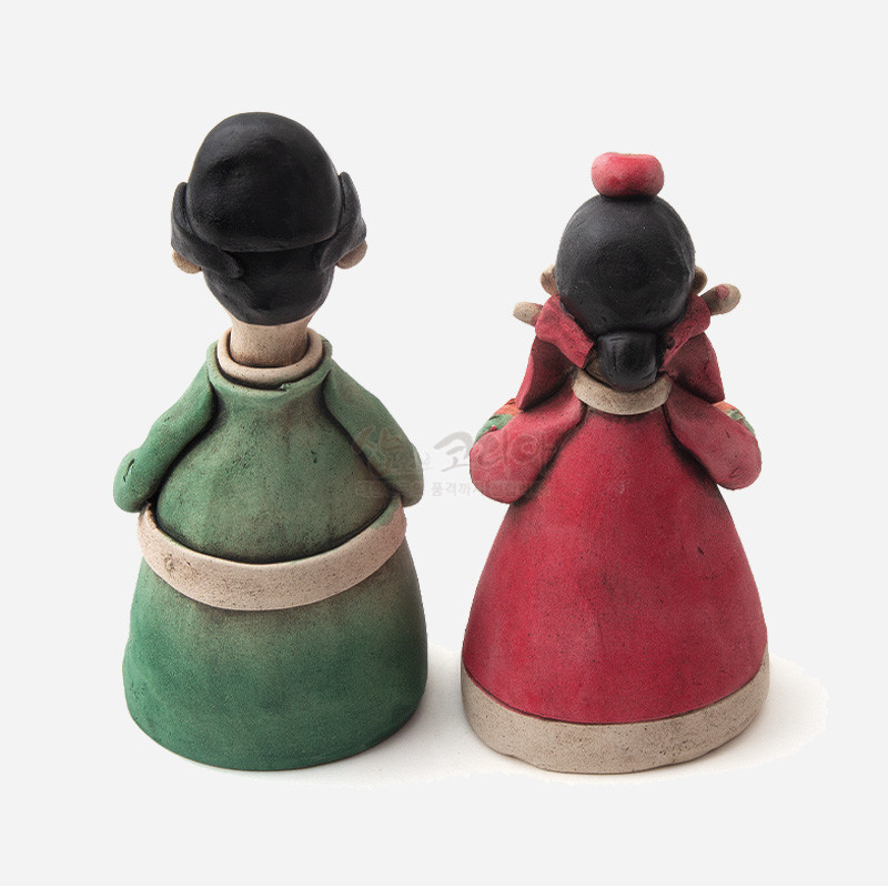 황토 재질로 제작된 전통 혼례복 신랑신부 인형, 녹색과 붉은색 의상 대비가 돋보이는 공예품. 황토 재질로 제작된 전통 혼례복 신랑신부 인형, 녹색과 붉은색 의상 대비가 돋보이는 공예품.