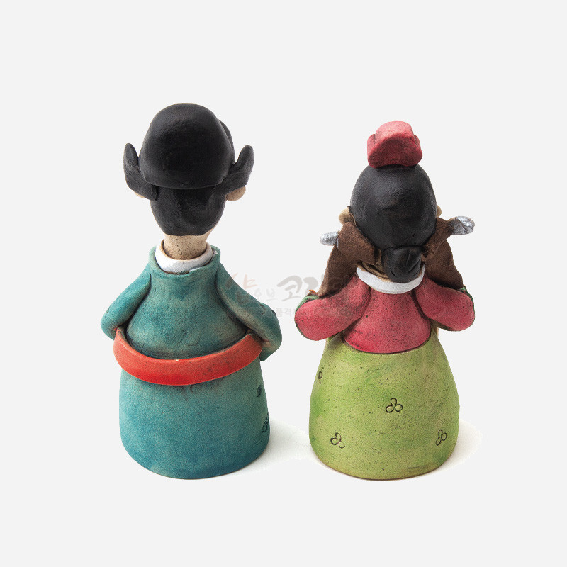 황토 재질로 빚은 전통 혼례 신랑신부 인형, 청록·연두 한복과 붉은 띠, 소박한 꽃문양 색채 대비가 특징인 장식품.