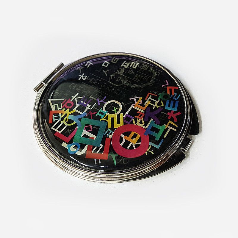 검은 바탕 위에 다채로운 색상의 한글 자음도 문양이 인쇄된 금속 테두리 손거울.