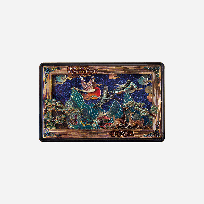 금속 재질에 입체 부조 기법으로 표현한 산수와 해, 학, 사슴의 십장생도 문양, 청록과 적색 대비가 돋보이는 직사각형 마그넷.