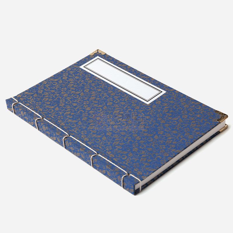 청색 비단 표지에 금색 전통 문양을 넣고 오침 제본과 금속 모서리 장식을 더한 노트.