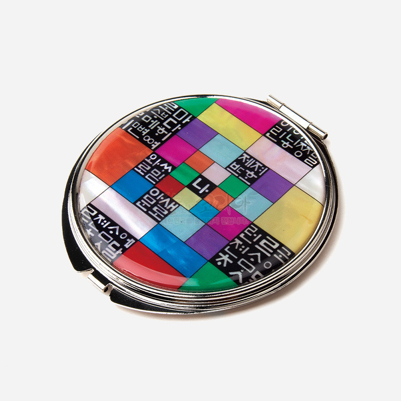 자개와 금속 재질로 제작된 손거울, 조각보 기법의 다채로운 색면과 흑백 훈민정음 문자 문양이 특징인 디자인.