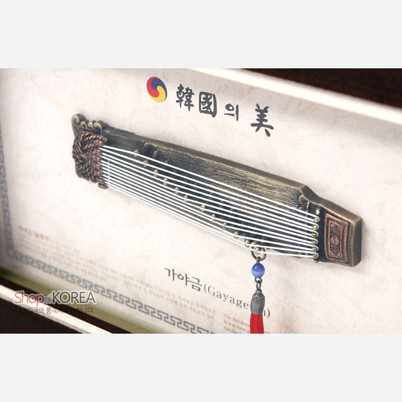 금속 재질의 가야금 모형과 흰 줄 장식, 파란 구슬과 붉은 술 노리개가 조화를 이룬 전통 악기 액자형 장식.