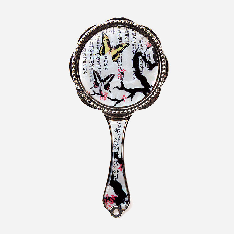 자개 느낌의 광택 위에 한글 서체와 매화 가지, 나비 문양을 담은 금속 손잡이 장식 손거울.