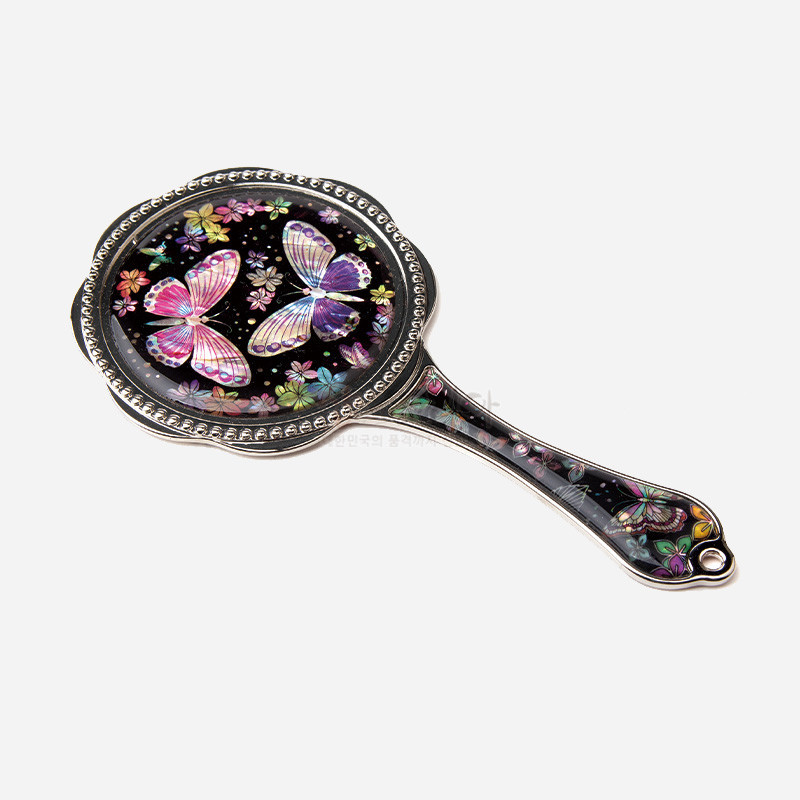 흑색 바탕 위 자개 상감으로 표현된 화려한 꽃과 나비 문양, 금속 테두리 장식이 조화를 이룬 손잡이 거울.