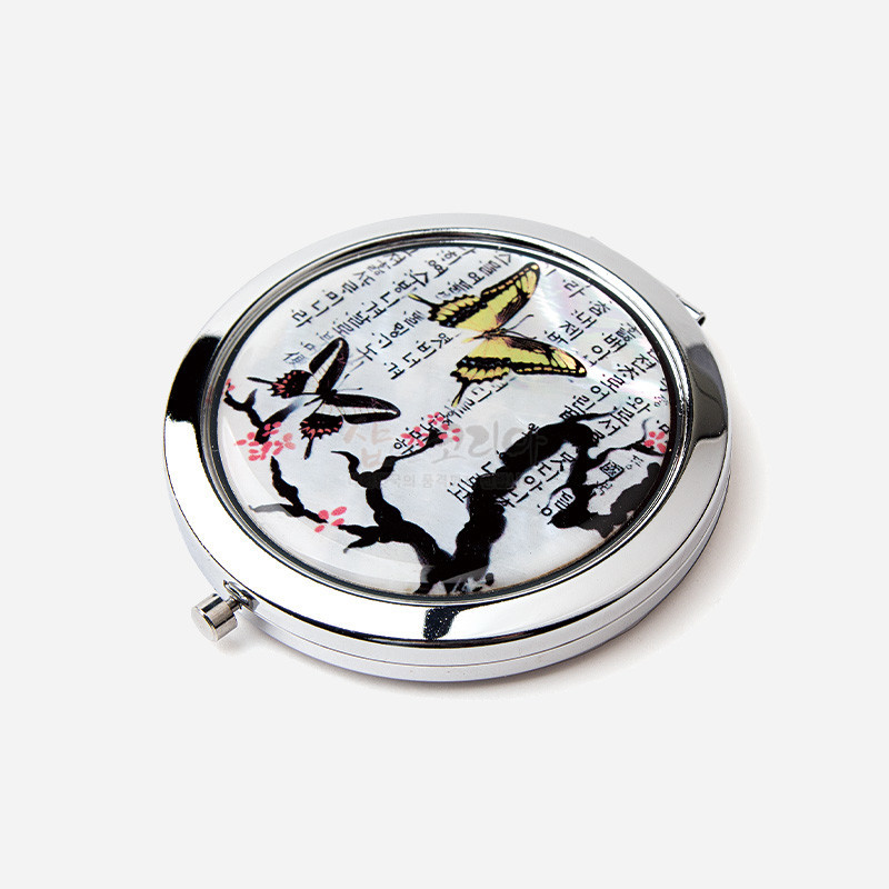 자개 바탕 위에 매화나무와 나비, 한글 서체 문양을 담은 원형 금속 테두리 손거울.