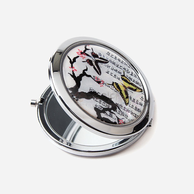 자개 장식 금속 손거울, 한지 느낌 바탕에 매화 가지와 나비 문양, 은색과 노랑·분홍 대비가 특징인 디자인.