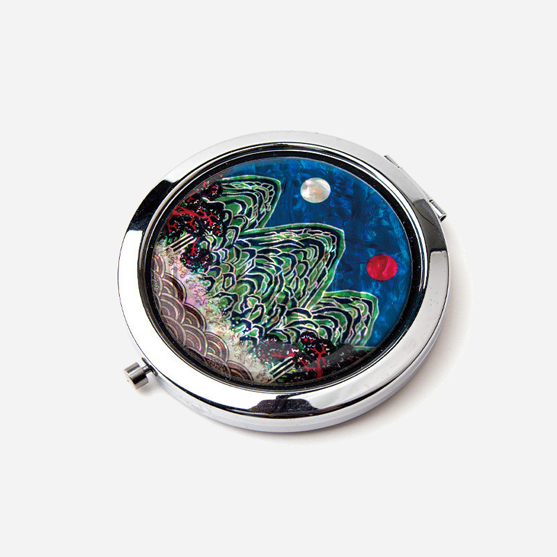 자개 상감 기법으로 일월오봉도 산수문을 표현한 원형 금속 손거울, 푸른 바탕 위 다채로운 색감과 광택이 돋보이는 디자인.