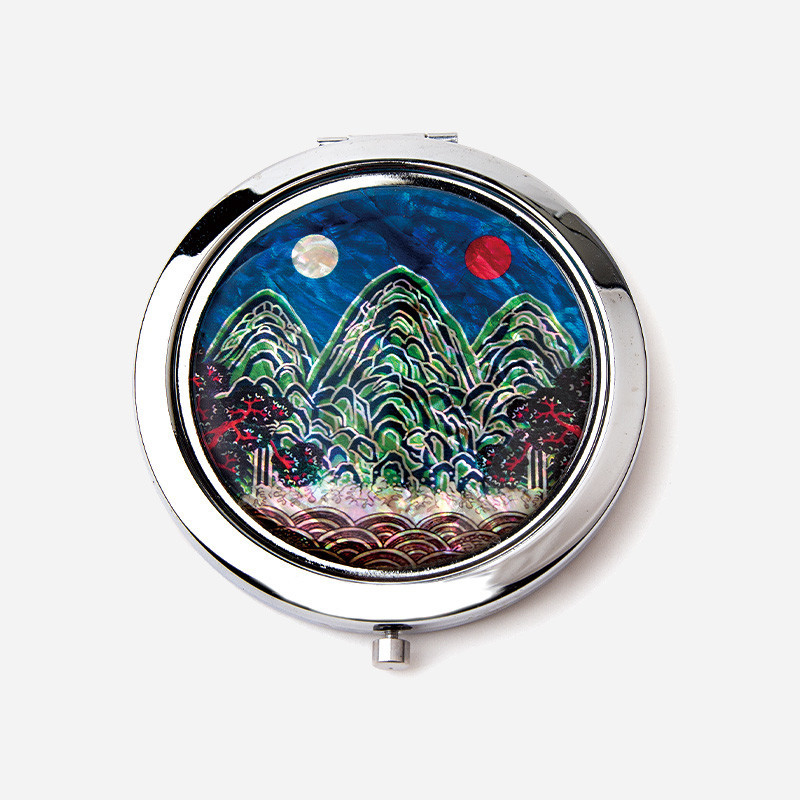 금속 테두리에 자개 상감 기법으로 표현한 청록색 산과 일월오봉도 문양이 돋보이는 원형 손거울.