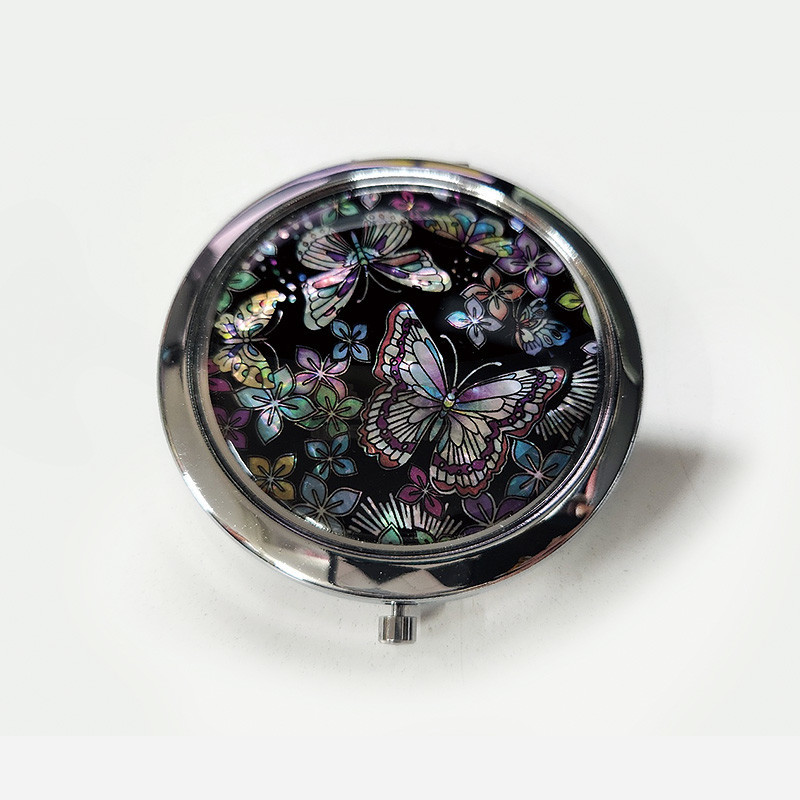 검은 바탕 위에 오색 자개 상감으로 꽃과 나비 문양을 넣은 금속 테두리 둥근 손거울.