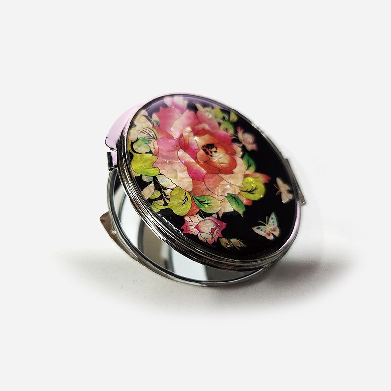 흑색 바탕 위 자개 상감 기법으로 장미와 나비 문양을 넣은 원형 금속 손거울.