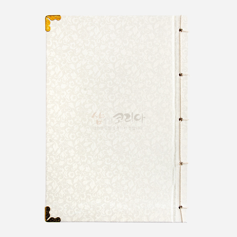 크림색 비단에 은은한 꽃넝쿨 문양을 넣고, 가장자리에 금속 모서리 장식과 끈 매듭 제본이 특징인 한글 자개오침노트.