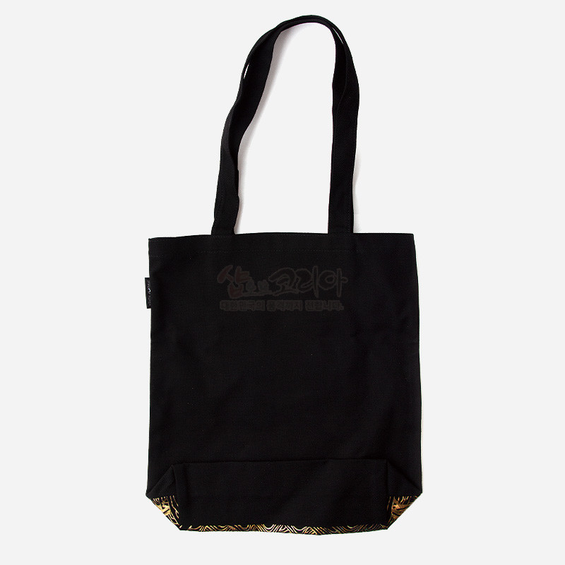 검정색 캔버스 천으로 제작된 에코백, 바닥 부분에 금색 기하학 문양 패브릭이 포인트인 디자인.