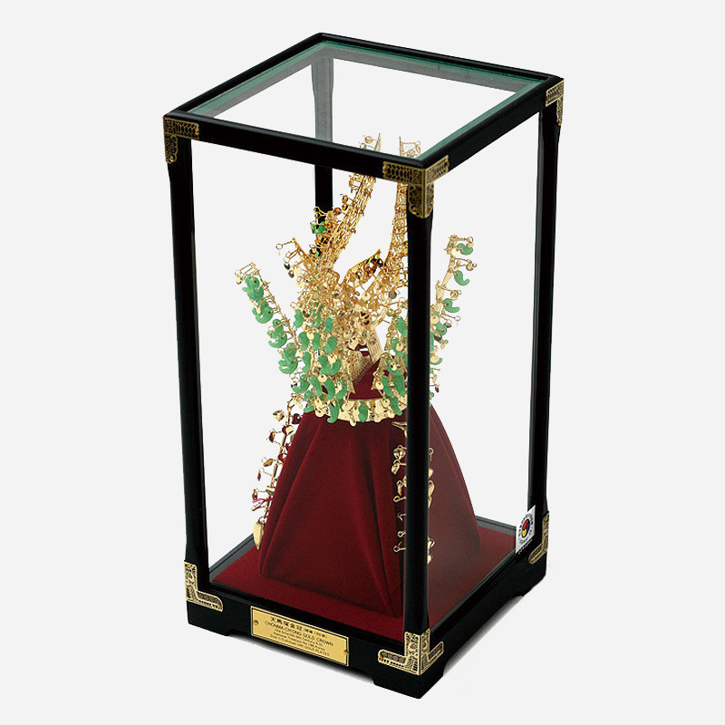 금색 금속과 옥색 장식으로 표현한 천마총 금관 모형, 유리 장식 케이스와 적색 천 받침대 구성.
