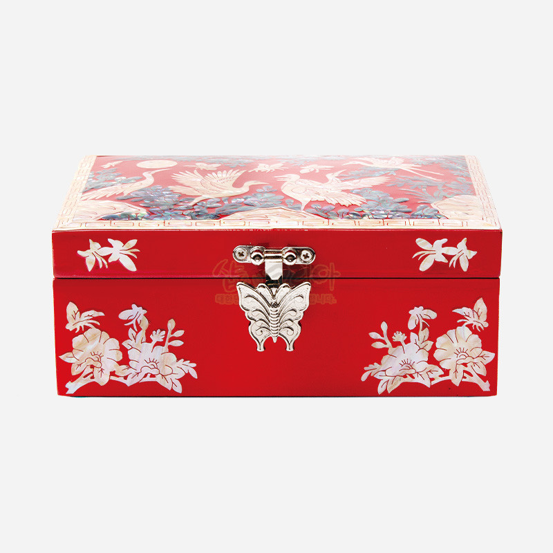 붉은 옻칠 바탕에 자개 상감 기법으로 학과 꽃, 나뭇가지 문양을 장식하고 은색 나비 모양 금속 잠금장치를 더한 직사각 보석함.