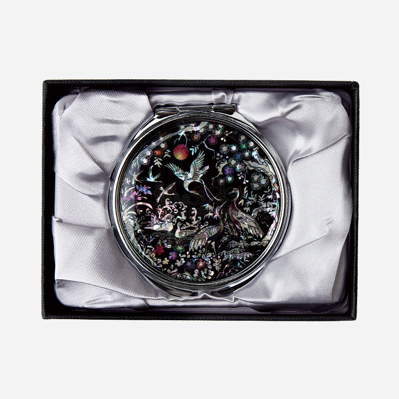 자개 상감 기법으로 학과 소나무, 꽃 문양을 넣은 검은 바탕의 금속 테두리 손거울.