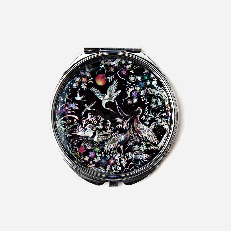 검은 옻칠 바탕에 자개 상감으로 소나무와 학, 파도와 꽃 문양을 정교하게 표현한 원형 금속 손거울.