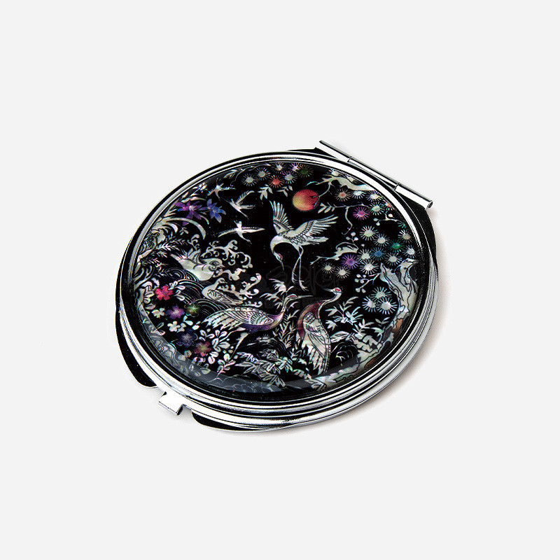 흑색 옻칠 바탕에 자개 상감 기법으로 송학과 꽃, 구름 문양을 섬세하게 표현한 금속 테두리 손거울.