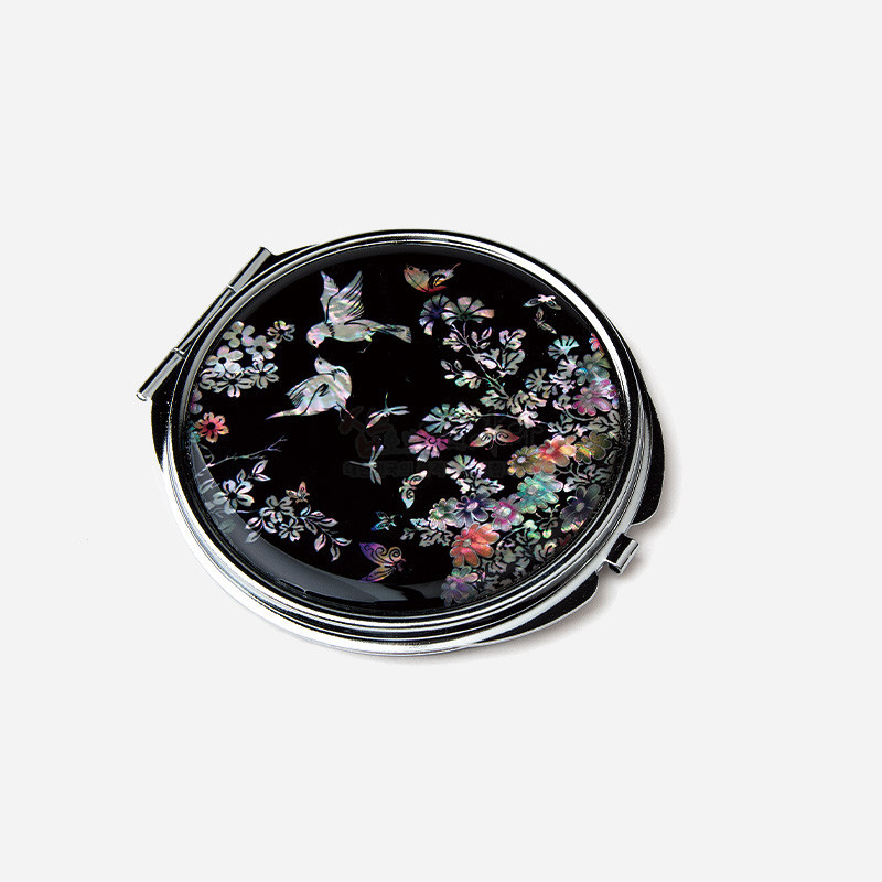 검은 바탕 위에 자개 상감 기법으로 화조도 문양을 섬세하게 표현한 원형 금속 손거울. 검은 바탕 위에 자개 상감 기법으로 화조도 문양을 섬세하게 표현한 원형 금속 손거울.