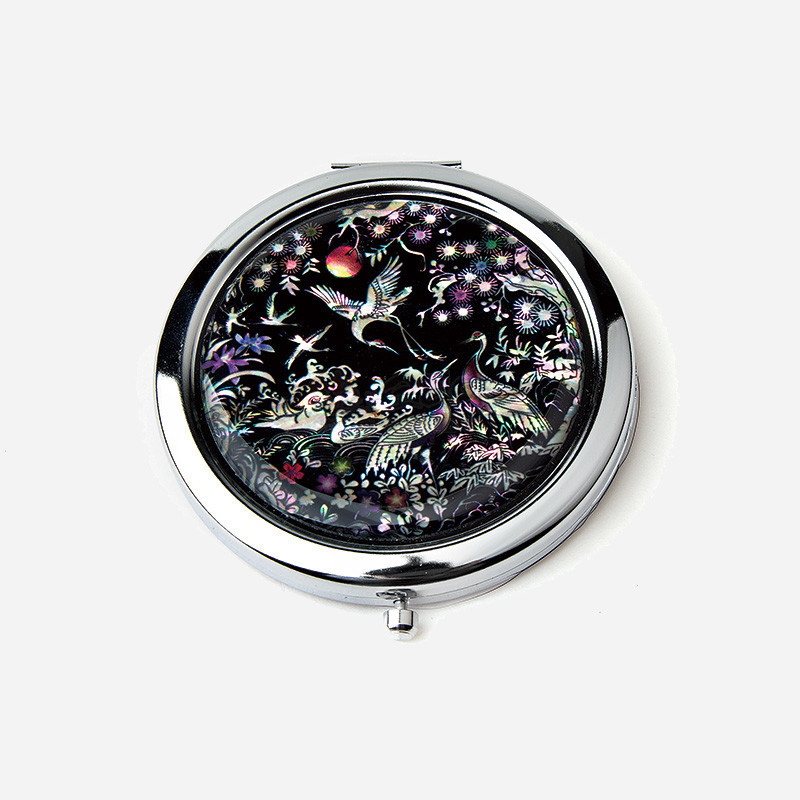 자개 상감 기법으로 흑색 바탕 위에 학과 소나무, 꽃과 과실 문양을 섬세하게 새긴 금속 테두리 원형 손거울.